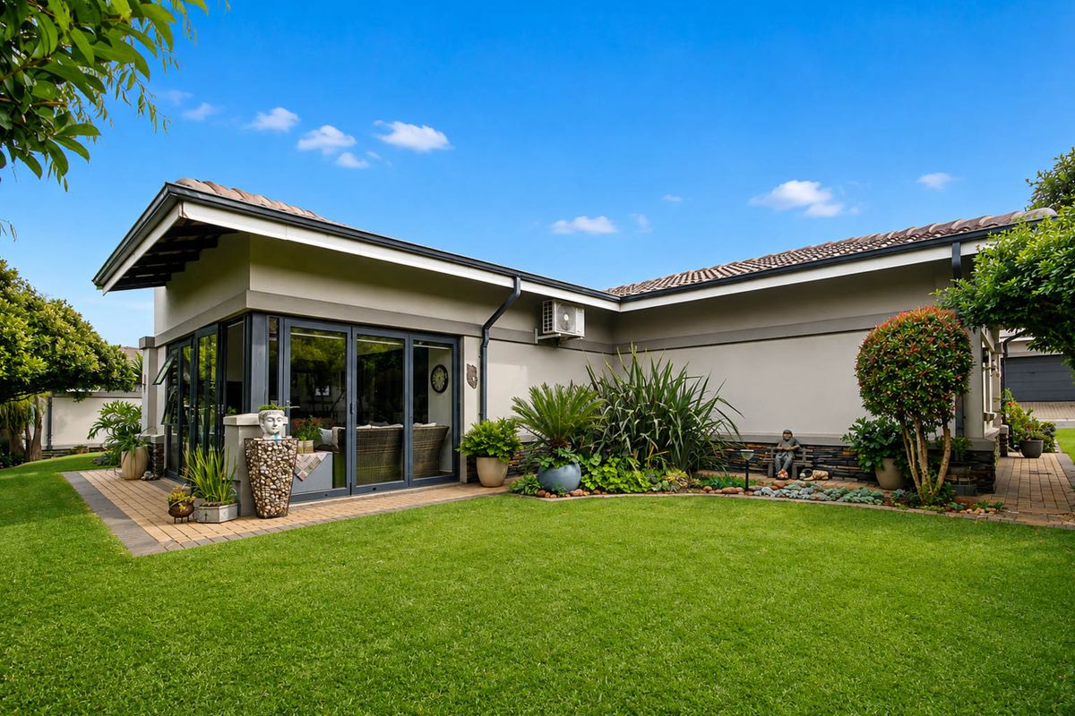 Well-maintained rear exterior featuring a paved patio, sliding glass doors, and landscaped garden area with stone cladding accents.