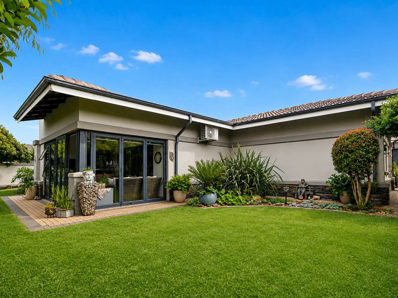 Well-maintained rear exterior featuring a paved patio, sliding glass doors, and landscaped garden area with stone cladding accents.