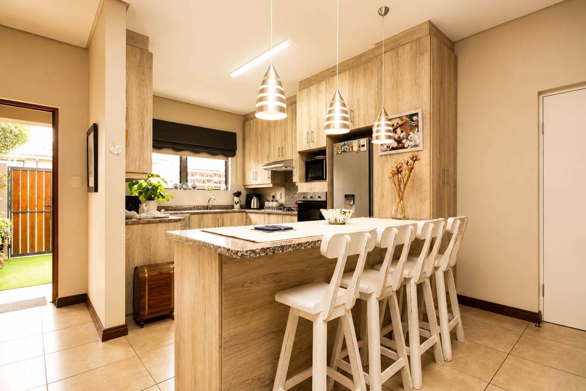 Modern kitchen featuring light wood-look cabinetry, granite countertops, built-in appliances, and a breakfast bar with pendant lighting, seamlessly connected to an outdoor patio area.