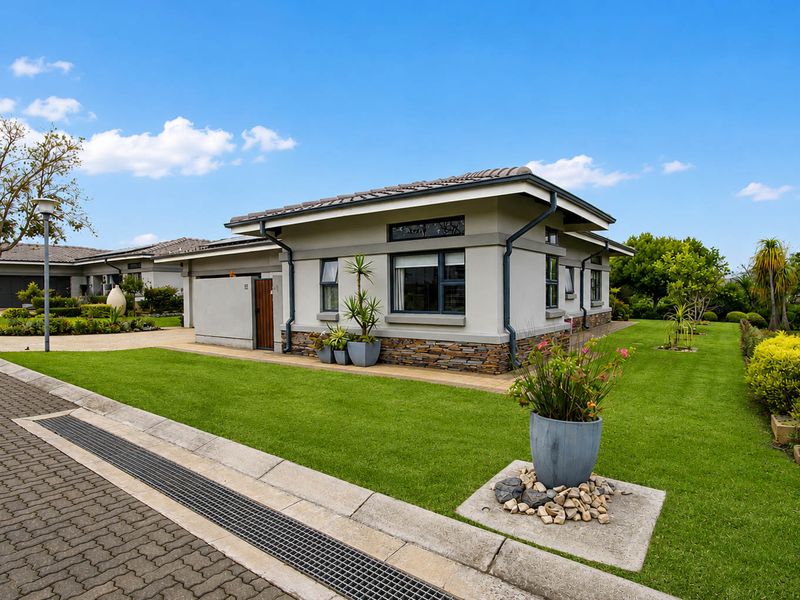 A well-maintained retirement village home featuring stone cladding, a tiled roof, and neatly landscaped garden surroundings.