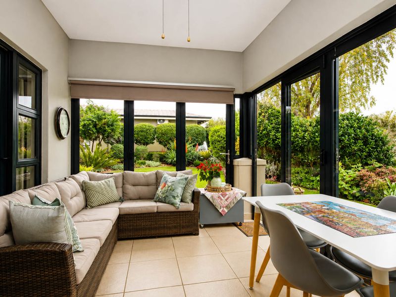 A bright and well-maintained enclosed patio featuring large black aluminium sliding doors that provide seamless access and views to the landscaped garden.