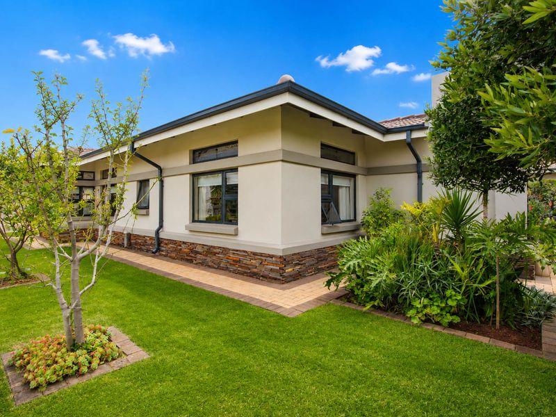 A well-maintained rear exterior view of the retirement unit featuring stone cladding, paved walkways, and established garden landscaping.