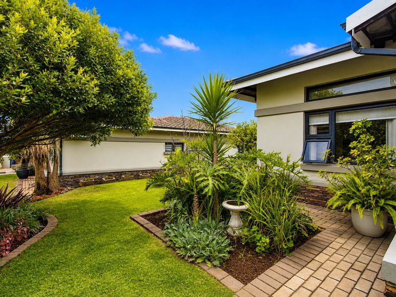 A well-maintained rear garden area featuring a paved walkway, established landscaping, and stone-clad exterior wall detailing.