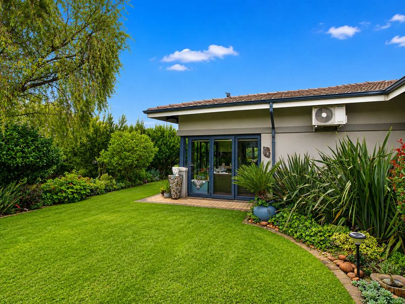 A well-maintained rear garden featuring a paved patio area, bi-fold doors leading into the home, and established landscaping.
