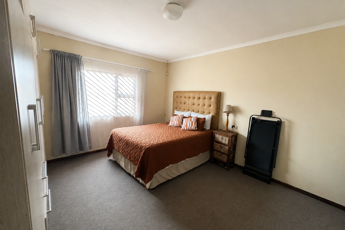 A functional bedroom featuring built-in cupboards, carpeted flooring, and security bars on the window, offering a neutral canvas for potential updates.