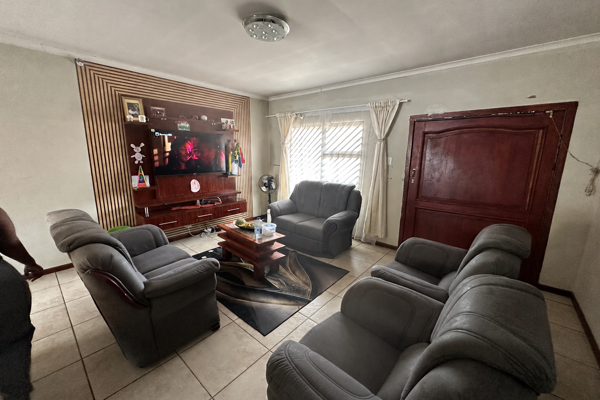 A living room featuring tiled flooring, a built-in media unit with decorative wall paneling, and a window with security bars.