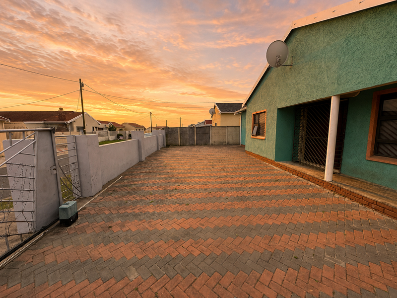 A paved front driveway and exterior facade of a residential property featuring a boundary wall and security gate at sunset.