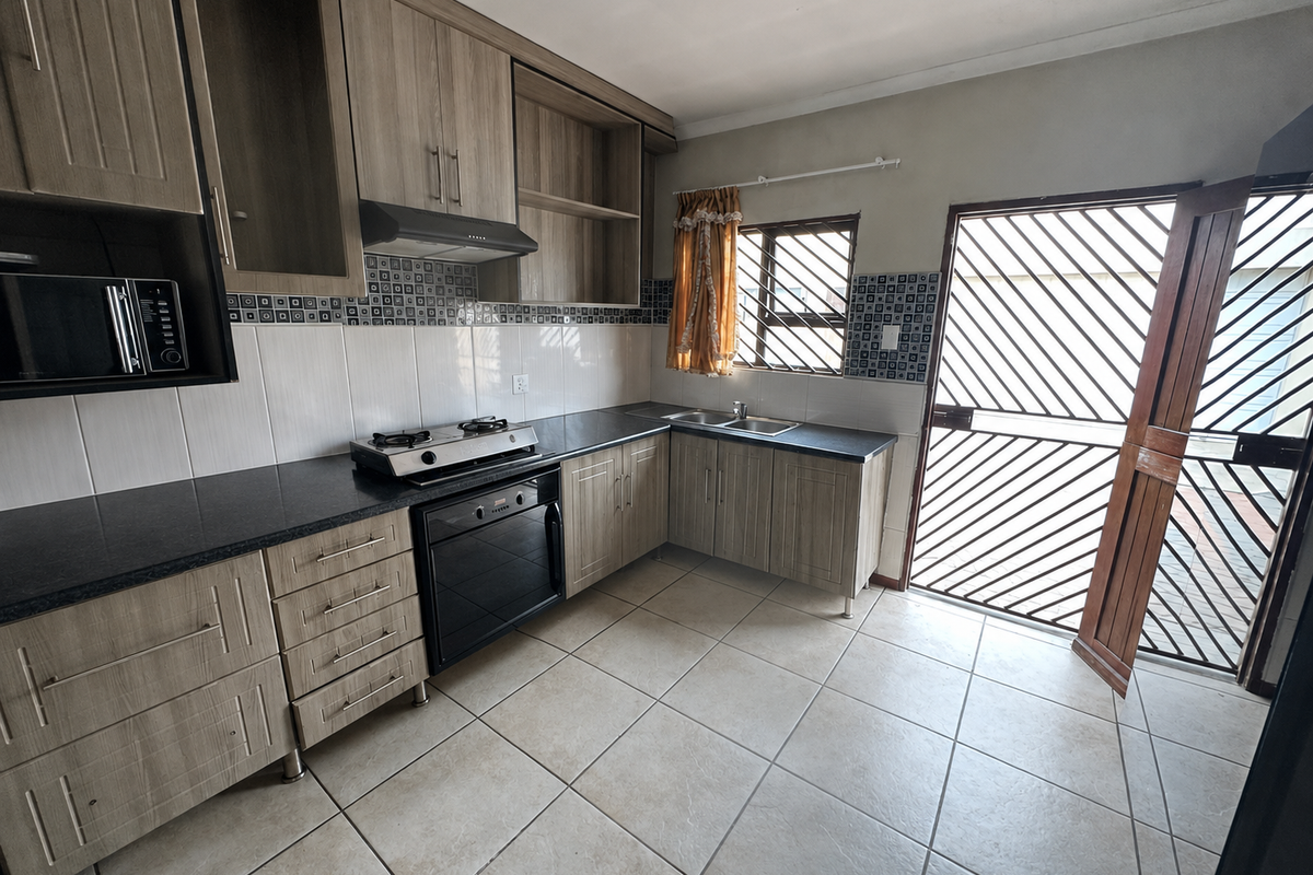Functional kitchen featuring wood-look cabinetry, dark laminate countertops, built-in oven with gas hob, and direct access to the exterior via a security gate.