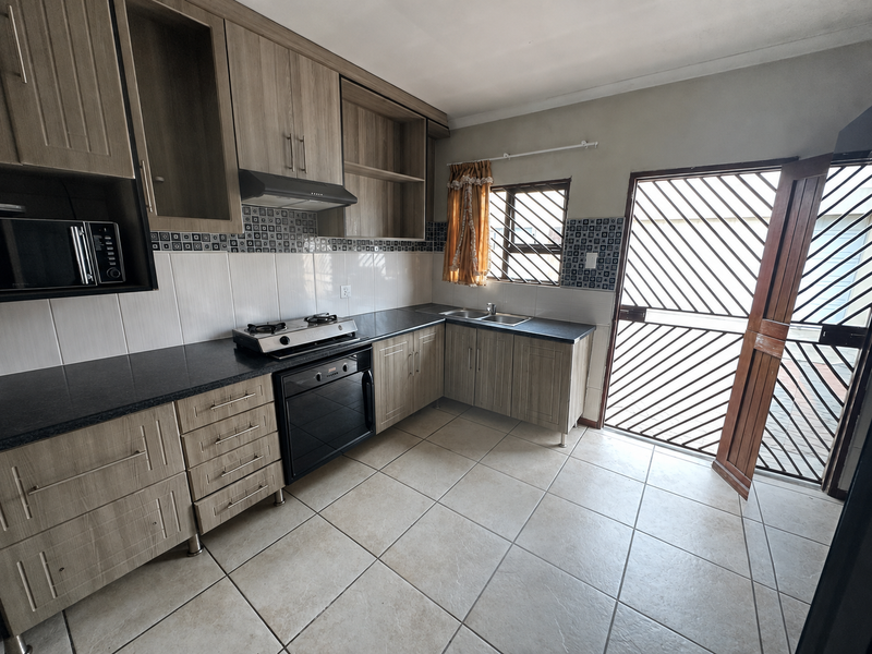 Functional kitchen featuring wood-look cabinetry, dark laminate countertops, built-in oven with gas hob, and direct access to the exterior via a security gate.