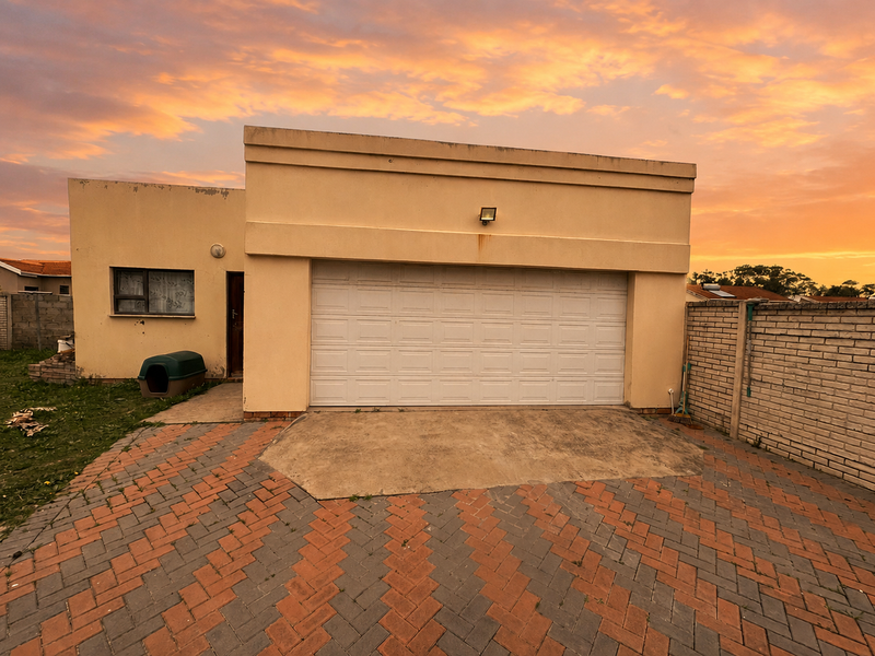 Exterior view of a single garage with a sectional door, paved driveway, and brick boundary wall at sunset.