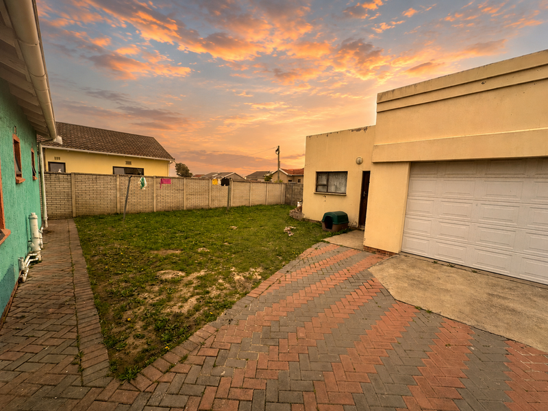 Rear exterior view featuring a brick paved driveway, a lawn area, and a garage with a white sectional door.