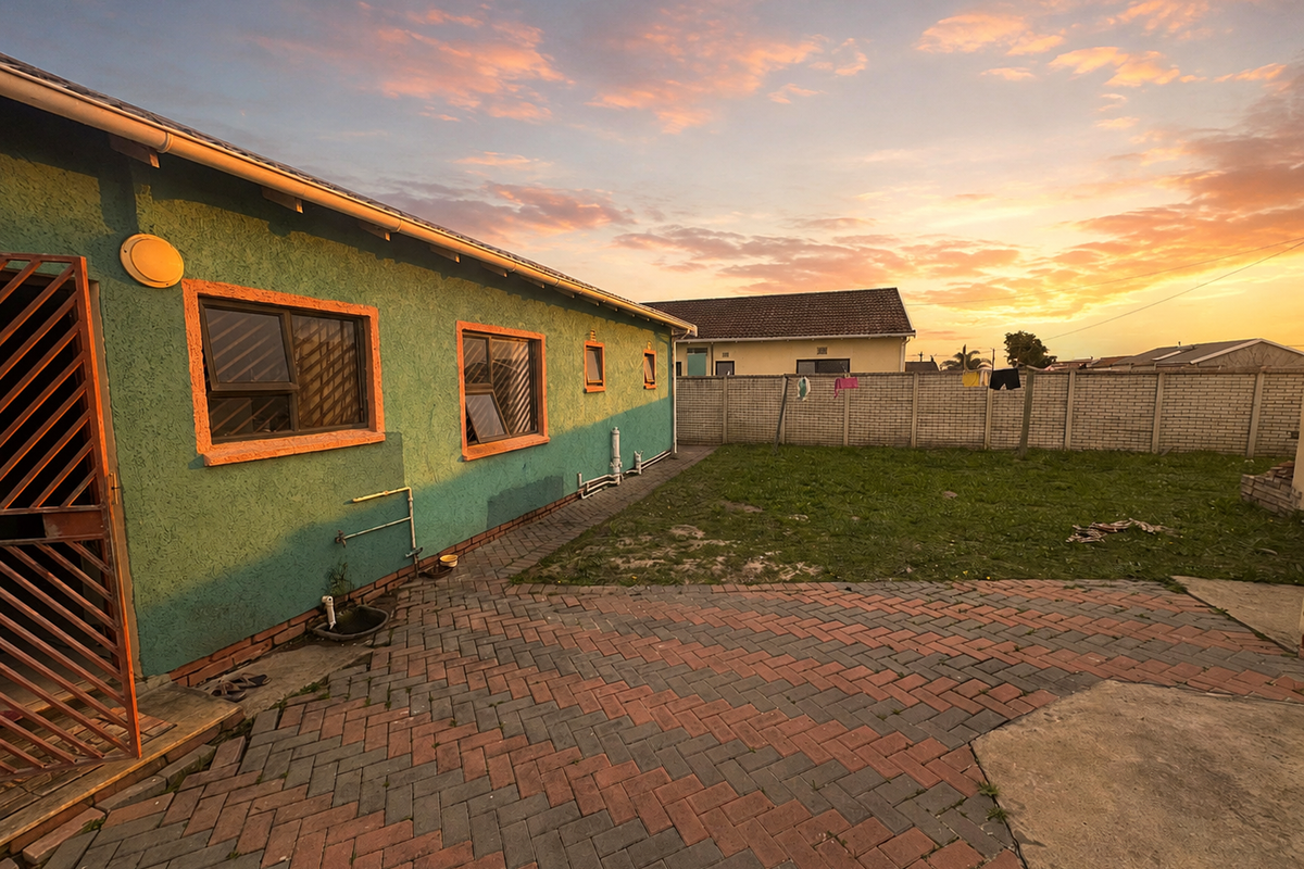 Rear exterior view featuring a paved patio area, perimeter wall, and access to the side of the house at sunset.