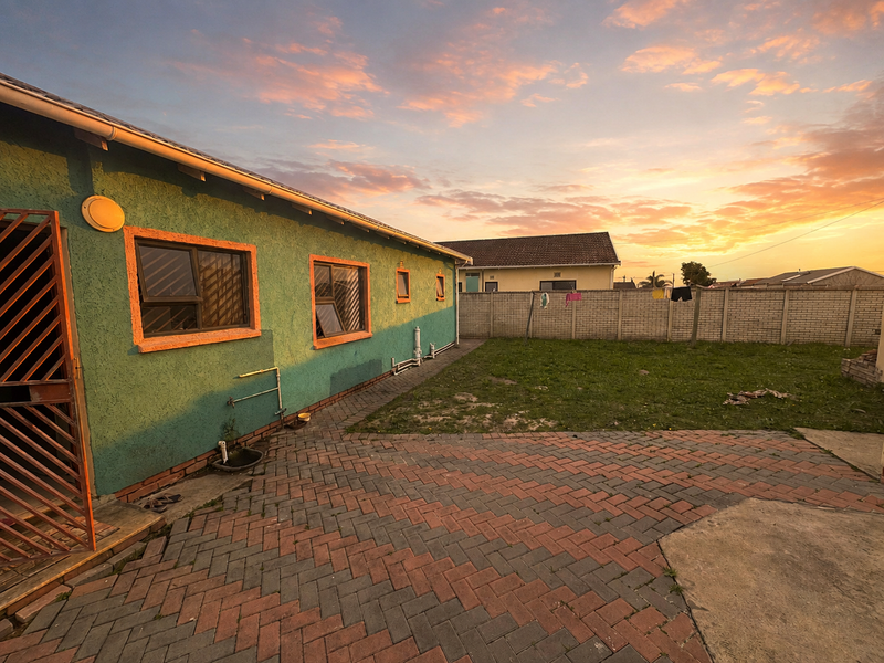 Rear exterior view featuring a paved patio area, perimeter wall, and access to the side of the house at sunset.