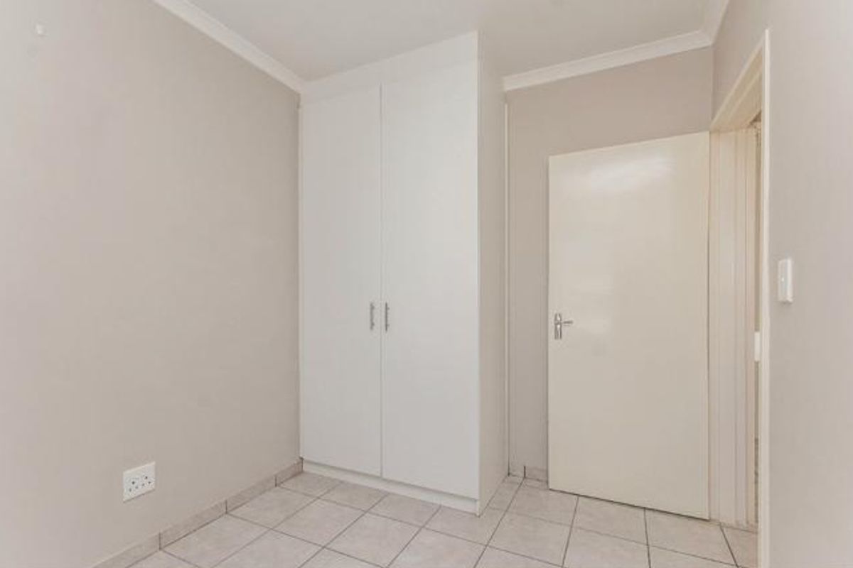 A clean, empty bedroom featuring neutral walls, tiled flooring, and a built-in wardrobe, offering a versatile space ready for personalization.