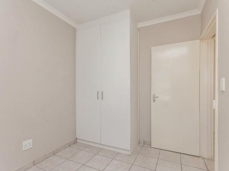 A clean, empty bedroom featuring neutral walls, tiled flooring, and a built-in wardrobe, offering a versatile space ready for personalization.