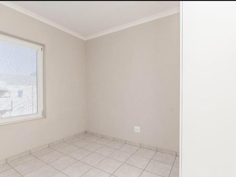 A clean, empty bedroom featuring neutral tiled flooring, a built-in cupboard, and a window fitted with blinds.
