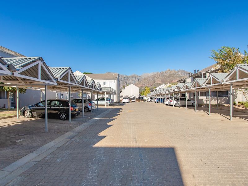 An outdoor parking area featuring multiple covered carports with metal roofing and paved ground surfaces, set within an apartment complex.