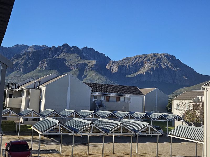 A scenic view of the apartment complex parking area featuring multiple carport structures with a prominent mountain range in the background.