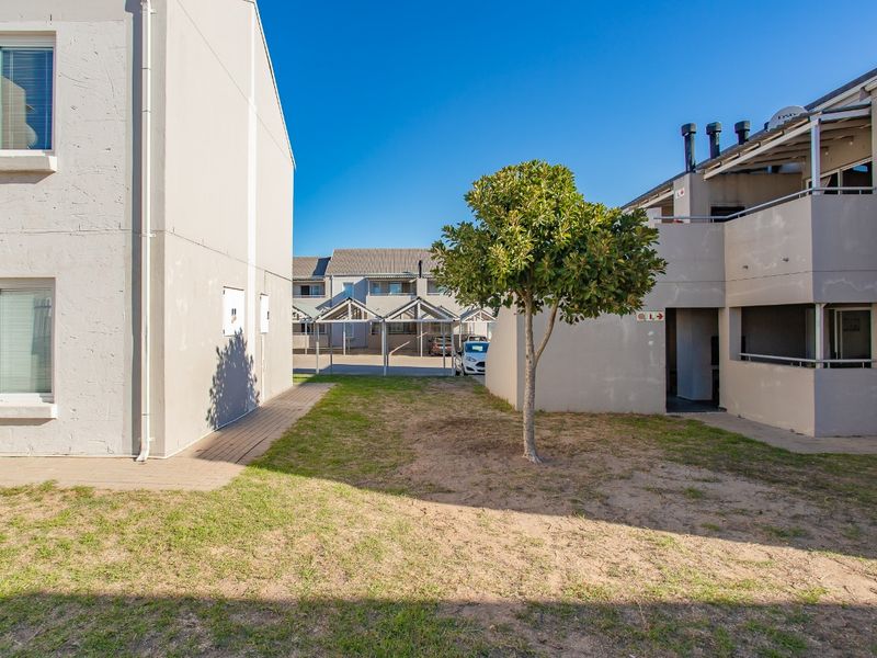 A view of the apartment complex exterior featuring a shared lawn area, paved walkways, and covered parking structures.