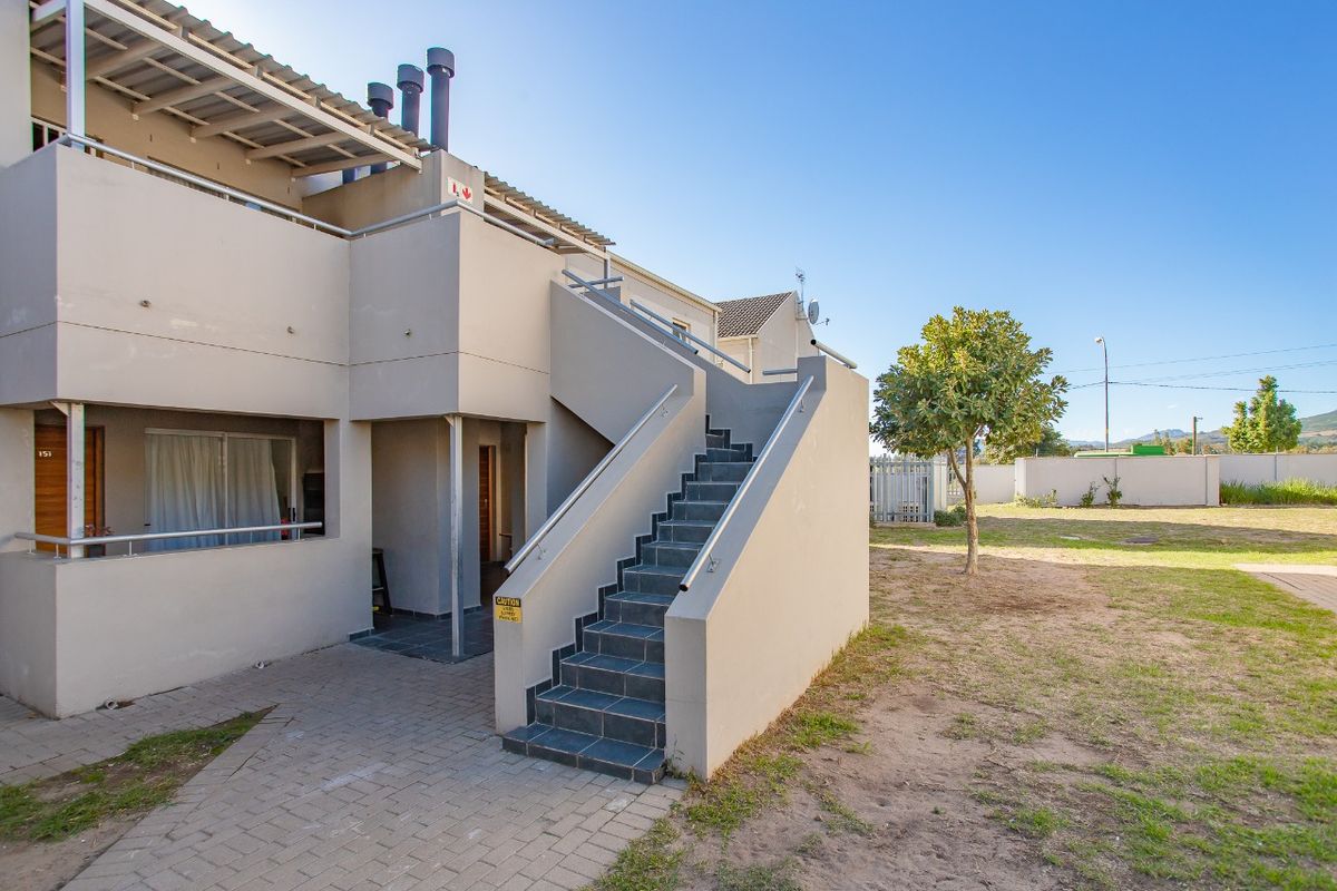 Exterior view of an apartment building featuring an external staircase, paved walkway, and balcony with metal railings.