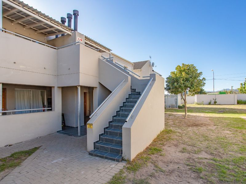 Exterior view of an apartment building featuring an external staircase, paved walkway, and balcony with metal railings.