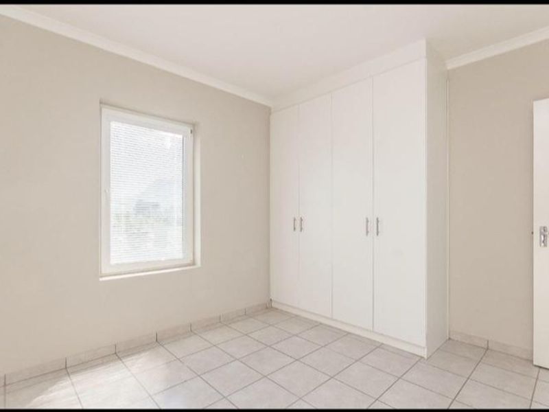 A clean, empty bedroom featuring neutral tiled flooring, built-in white cupboards, and a window with fitted blinds.