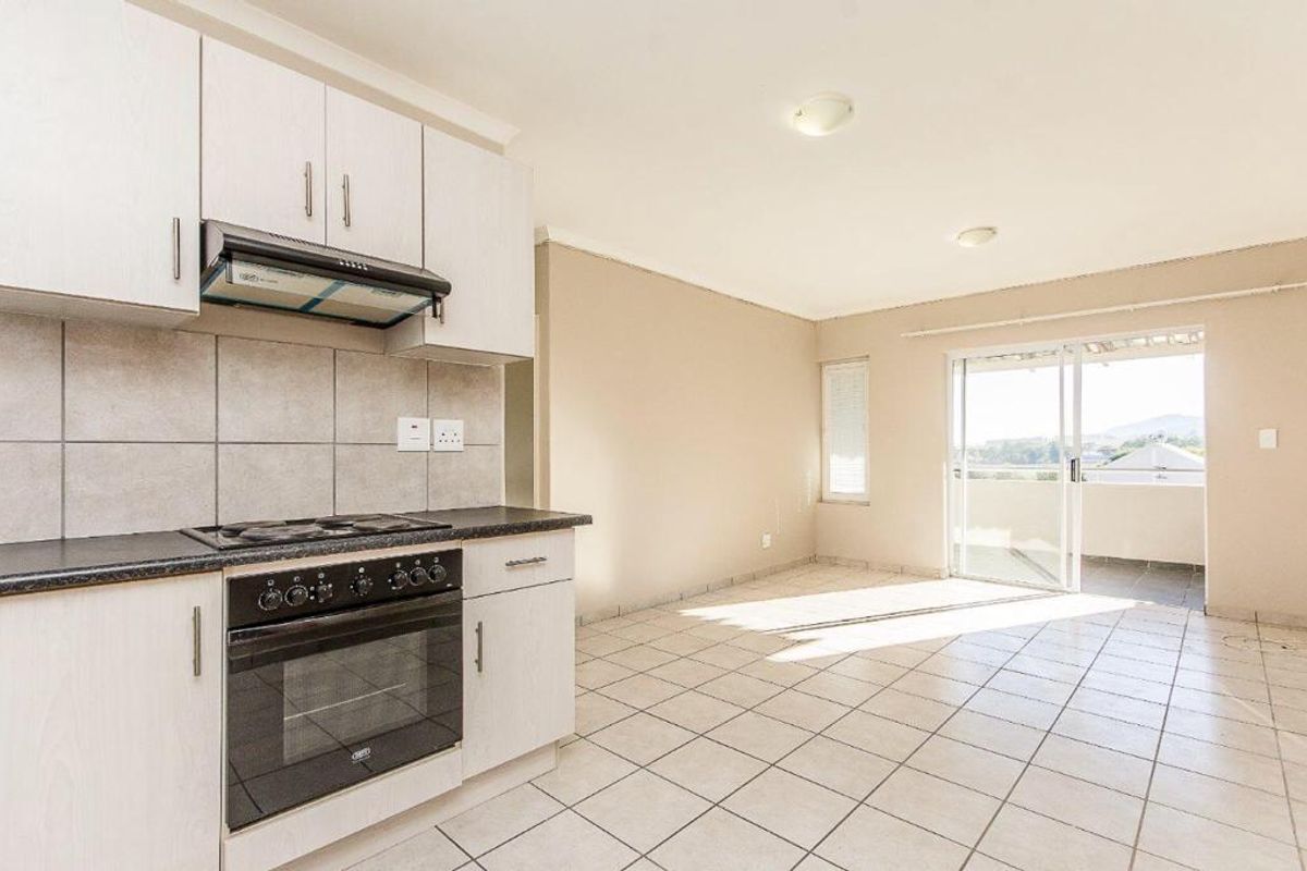 Open-plan kitchen and living area featuring tiled floors, built-in cabinetry, integrated oven and hob, and sliding door access to a balcony.