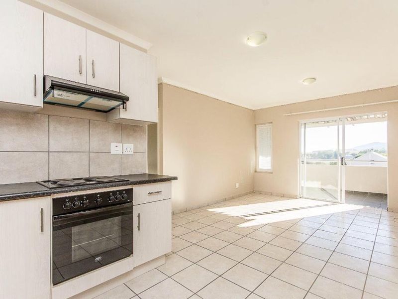 Open-plan kitchen and living area featuring tiled floors, built-in cabinetry, integrated oven and hob, and sliding door access to a balcony.