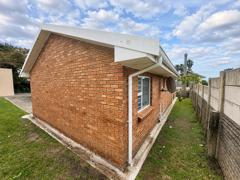 Rear exterior view of the townhouse featuring exposed brickwork, white guttering, security-barred windows, and a precast concrete boundary wall.