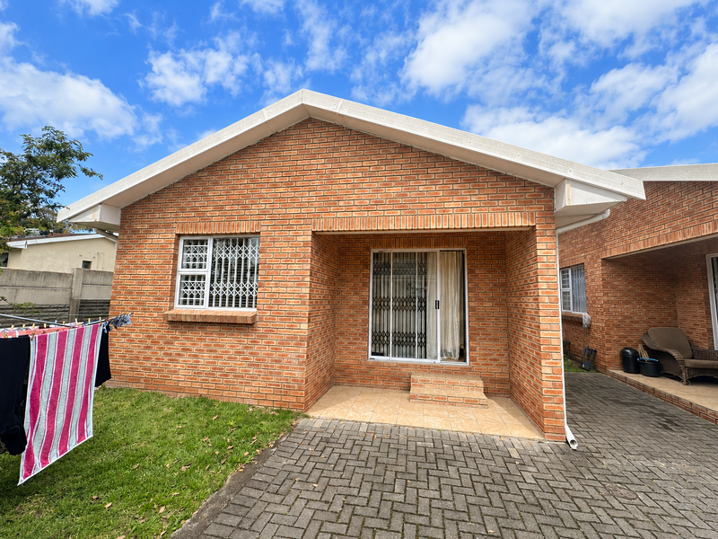 Rear view of a face brick townhouse featuring a paved driveway, a small tiled patio, and secure sliding door access.
