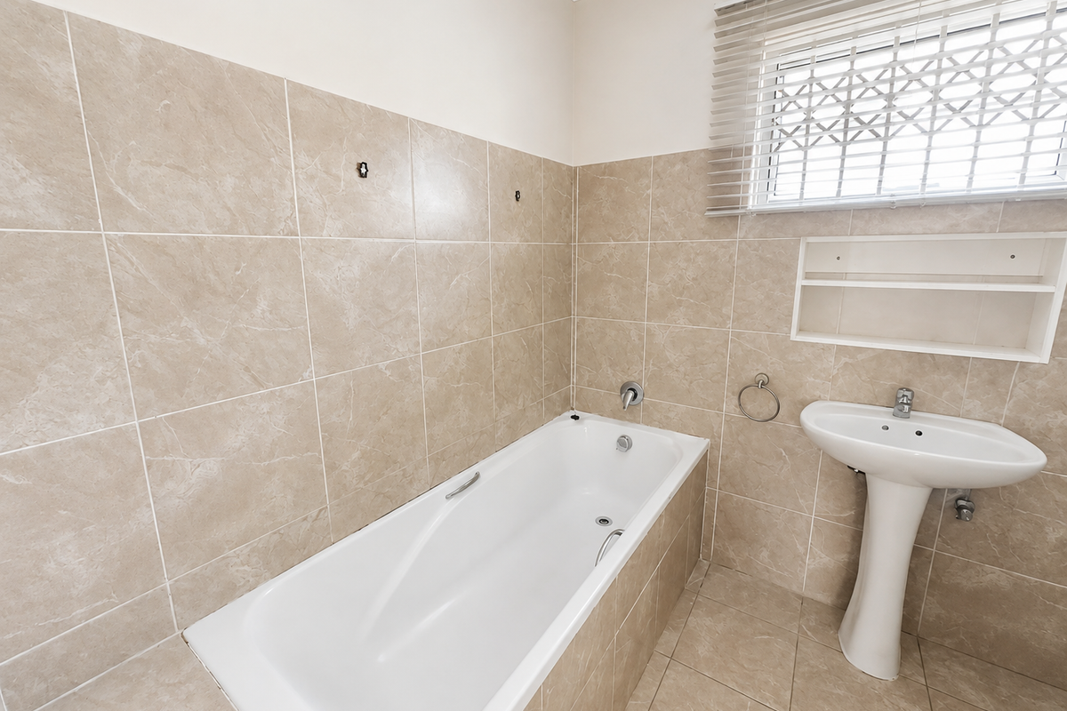 A clean, neutral-toned bathroom featuring a bathtub, pedestal basin, and tiled finishes, ready for personal touches or minor updates.
