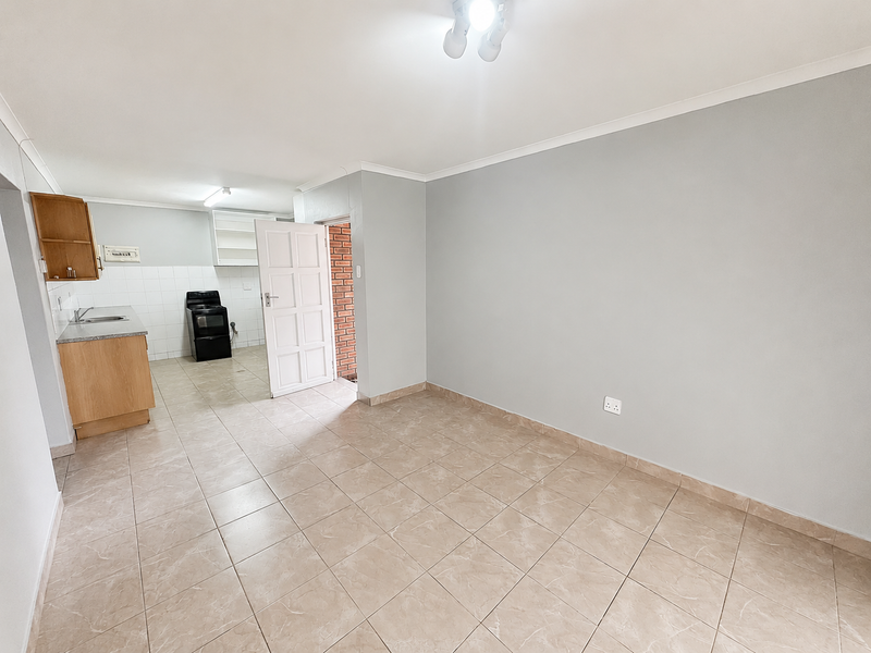 An open-plan living and kitchen area featuring tiled flooring, neutral walls, and a functional kitchen layout with built-in cabinetry and a freestanding stove.