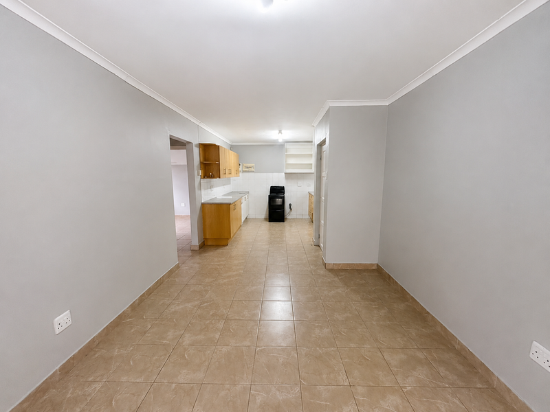 An empty kitchen area featuring tiled flooring, built-in wooden cabinetry, and a freestanding stove, offering a functional layout ready for personalization.