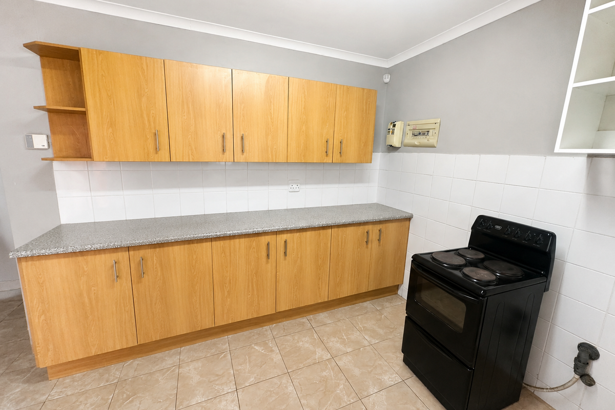 A clean, functional kitchen featuring light wood-finish cabinetry, a tiled backsplash, and a freestanding electric stove with neutral floor tiling.