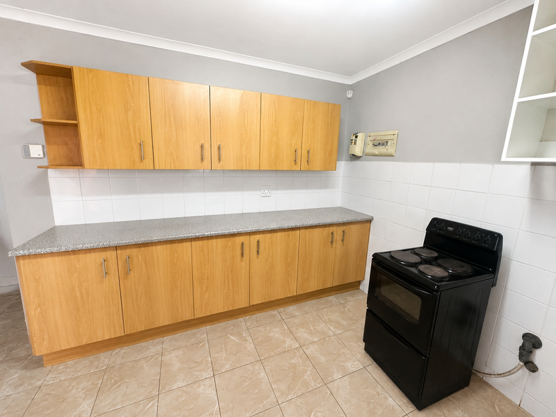A clean, functional kitchen featuring light wood-finish cabinetry, a tiled backsplash, and a freestanding electric stove with neutral floor tiling.