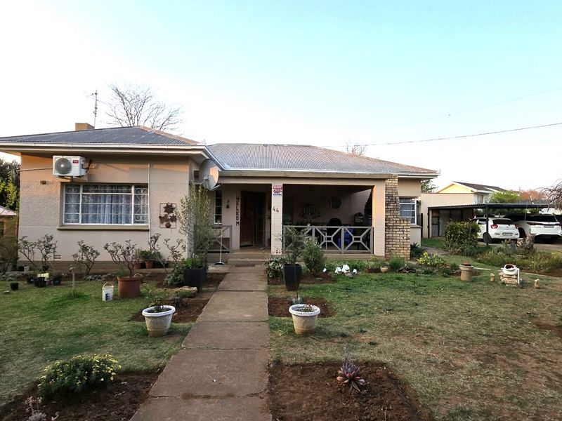 Front view of a single-story house featuring a covered patio, corrugated metal roof, and a paved walkway leading to the entrance.