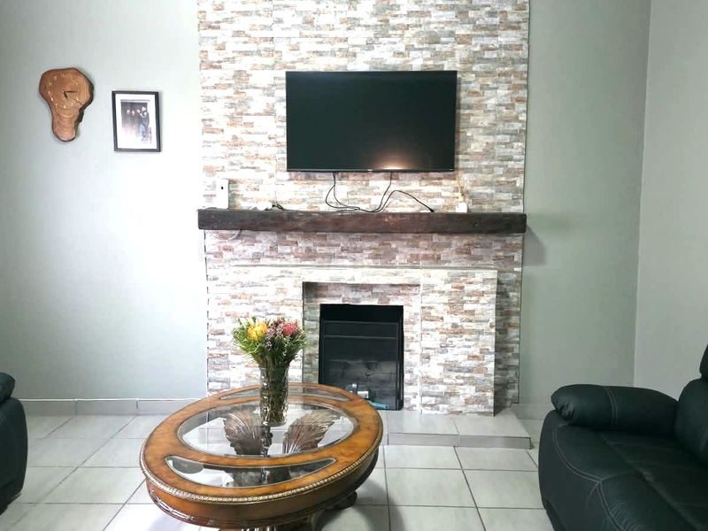A living room featuring a prominent stone-clad fireplace with a timber mantelpiece and neutral tiled flooring.