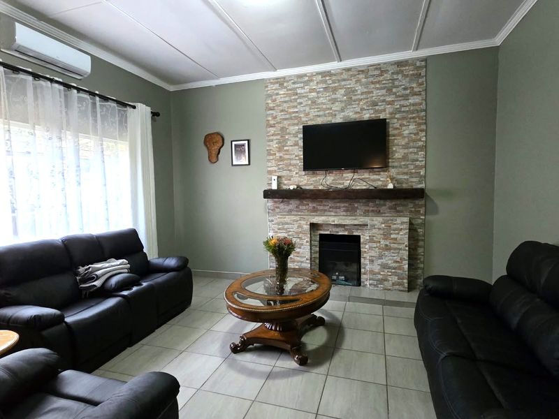 A comfortable living room featuring a stone-clad fireplace with a timber mantelpiece, tiled flooring, and a wall-mounted air conditioning unit.