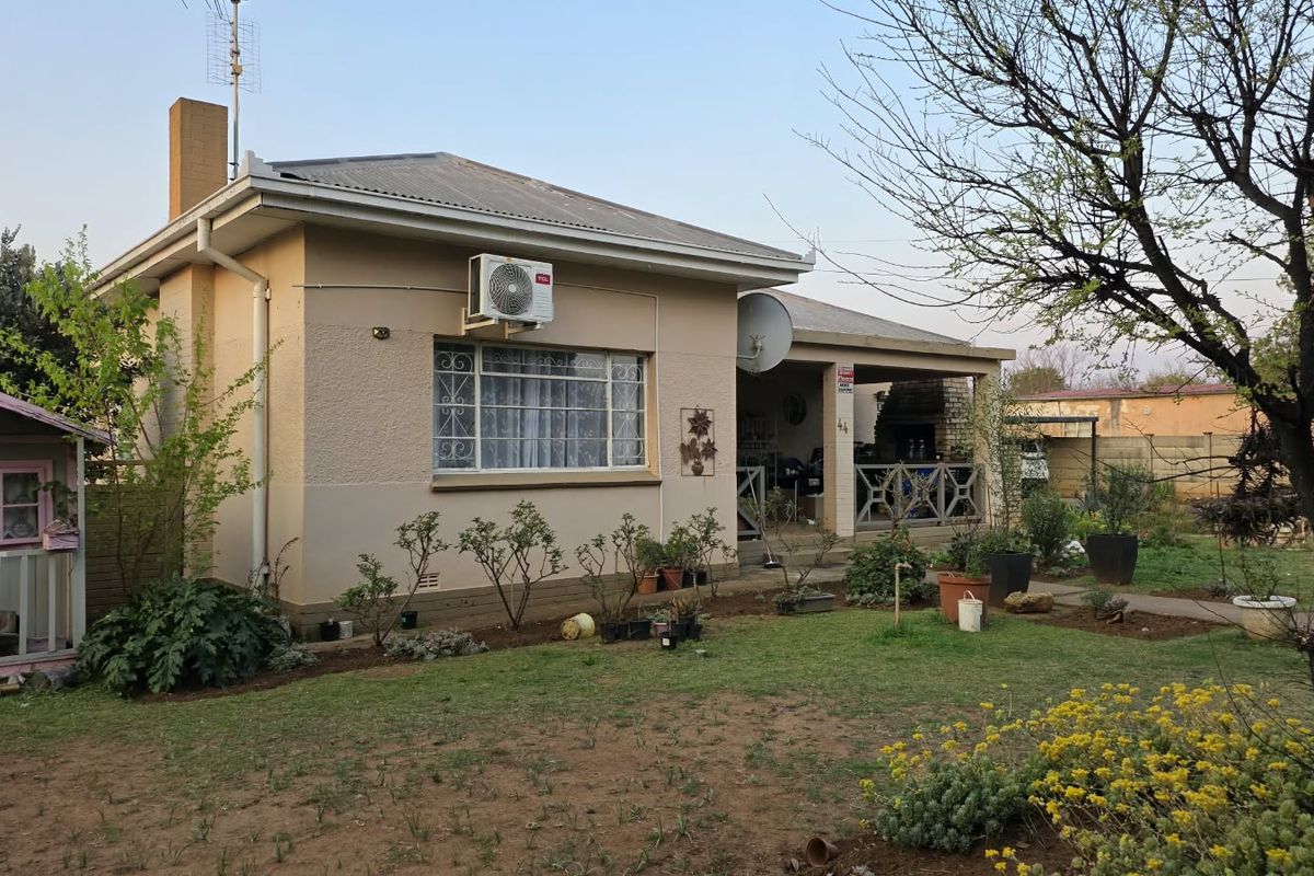 Rear view of the house featuring a covered patio, brick chimney, and established garden area with a lawn.