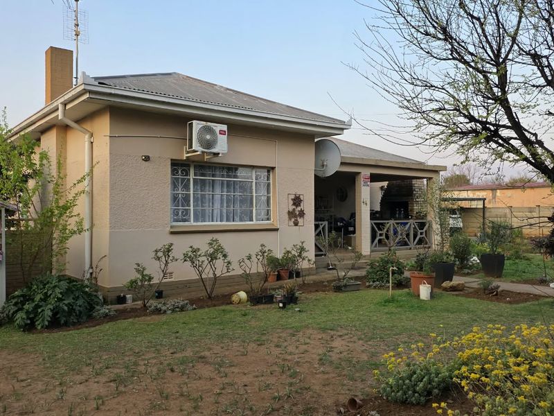 Rear view of the house featuring a covered patio, brick chimney, and established garden area with a lawn.