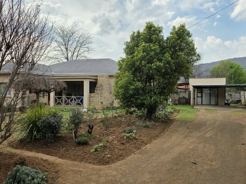 Front view of a single-story house featuring a covered patio, brick exterior, metal roofing, and a detached carport with an unpaved driveway.
