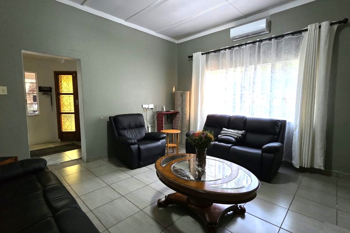 A comfortable living room featuring tiled flooring, a wall-mounted air conditioning unit, and access to an adjacent hallway.