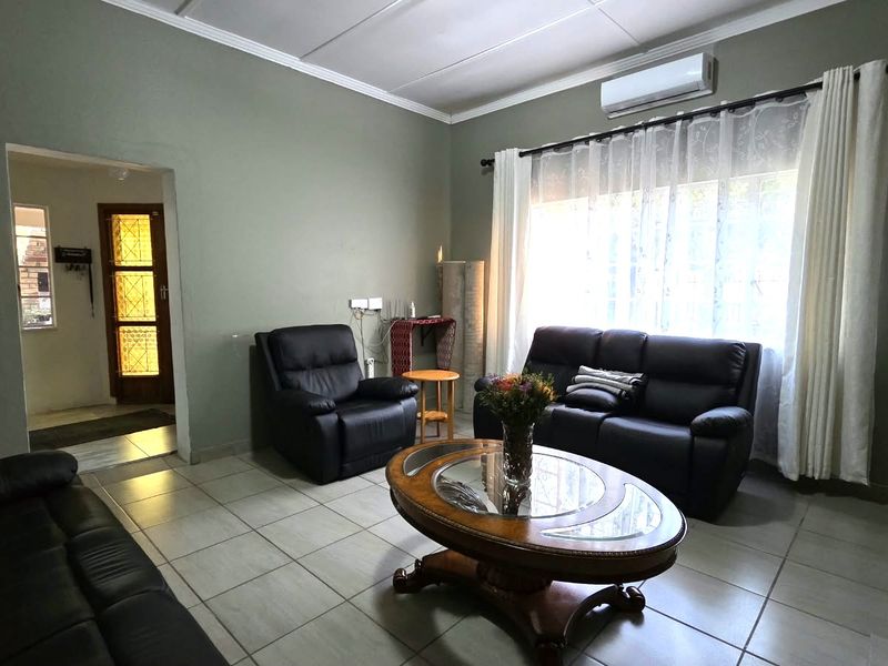 A comfortable living room featuring tiled flooring, a wall-mounted air conditioning unit, and access to an adjacent hallway.