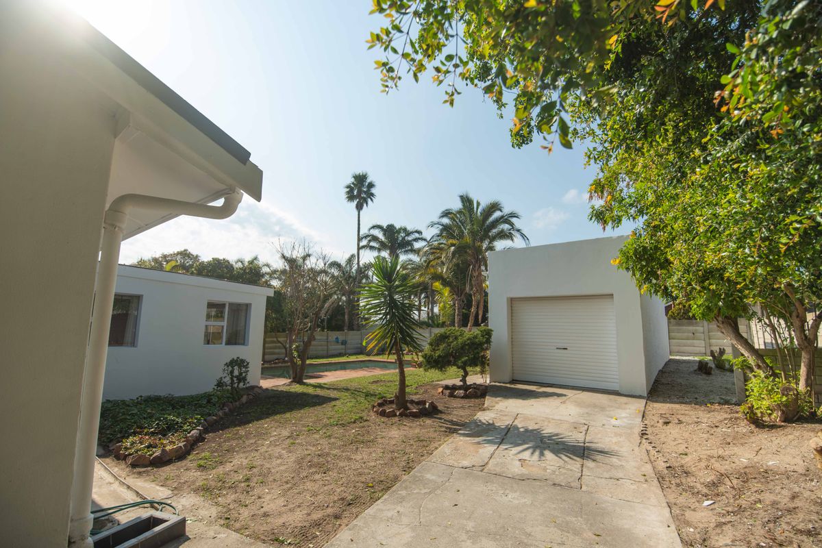 Rear garden view featuring a swimming pool, detached garage, and concrete driveway with established trees and boundary walling.