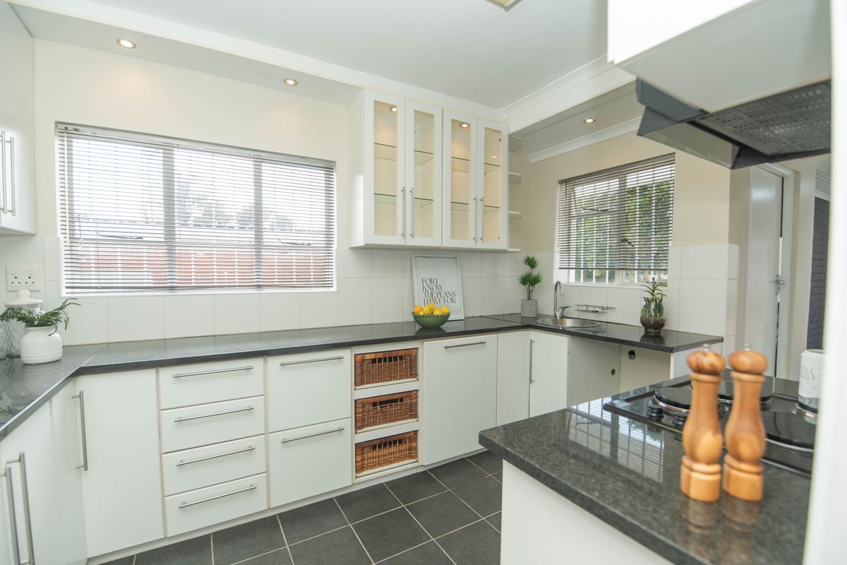 A well-maintained kitchen featuring white cabinetry, dark granite countertops, a gas hob, and integrated storage solutions with ample natural light.