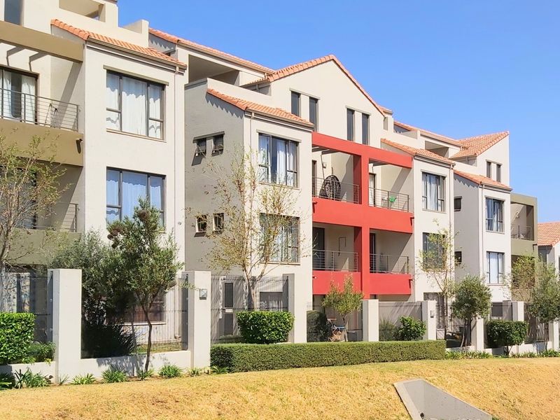 A modern multi-story apartment complex featuring terracotta roof tiles, private balconies, and well-maintained perimeter landscaping.