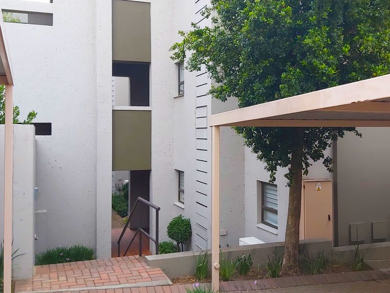 Exterior view of an apartment complex featuring a covered carport, paved walkways, and a staircase leading to the building entrance.