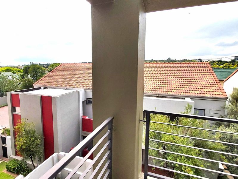 A covered balcony featuring a metal balustrade and concrete pillar, offering an elevated view of the surrounding residential complex.