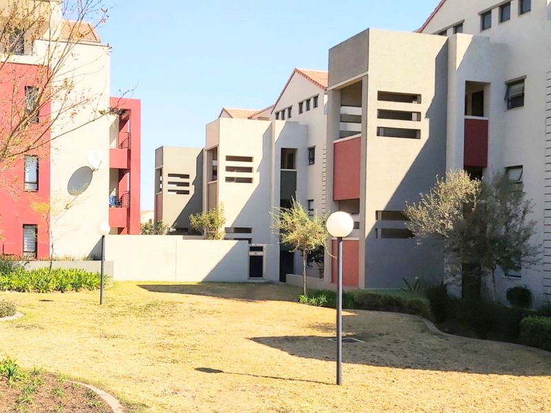 A view of the communal garden area and exterior facades of the apartment complex, featuring landscaped grounds and paved pathways.