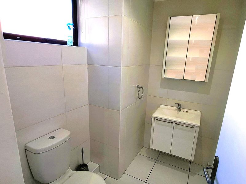 A clean, functional bathroom featuring a wall-mounted vanity with a mirrored cabinet, dual-flush toilet, and neutral ceramic tiling throughout.